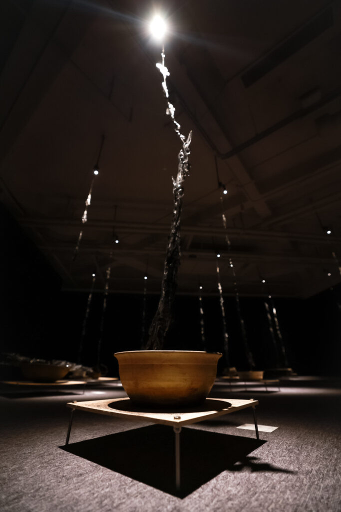 Installation view of “What Would You Say If You Could? #8: Against This Earth, We Knock” at How Art Museum, Shanghai. Resin, ashes (collected from JiangYong), motor, string, wooden platform, speakers, pan (collected from Jiangyong), 2023. Image courtesy of the artist.