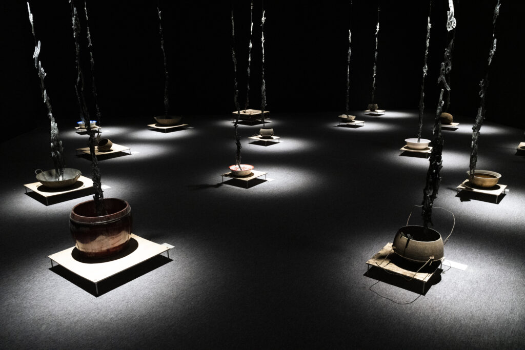 Installation view of “What Would You Say If You Could? #8: Against This Earth, We Knock” at How Art Museum, Shanghai. Resin, ashes (collected from JiangYong), motor, string, wooden platform, speakers, pan (collected from Jiangyong), 2023. Image courtesy of the artist.