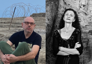 Dimitris Lyacos (left) sits with his knees to his chest in front of a barbed-wire fence. Toti O'Brien (right) stands with her arms crossed, chin tilted slightly upward at the camera.
