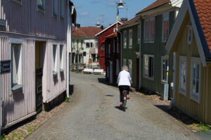 An older woman rides a bike down a street lined with colorful wooden buildings.