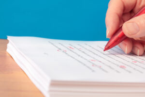 Hand with Red Pen Proofreading a Manuscript Closeup