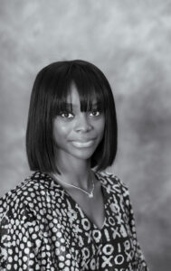 Ayotola Tehingbola's headshot: A woman with a dark bob and large eyes smiles inquisitively at the camera. The photograph is in black and white.