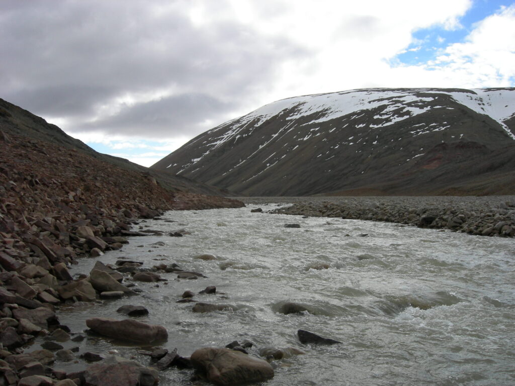 A close up a river on a rocky shore with a mountain in the distance.