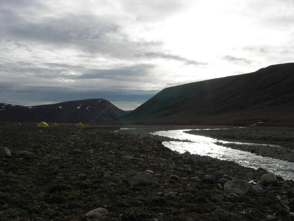 A rocky landscape with yellow tents in the distance.