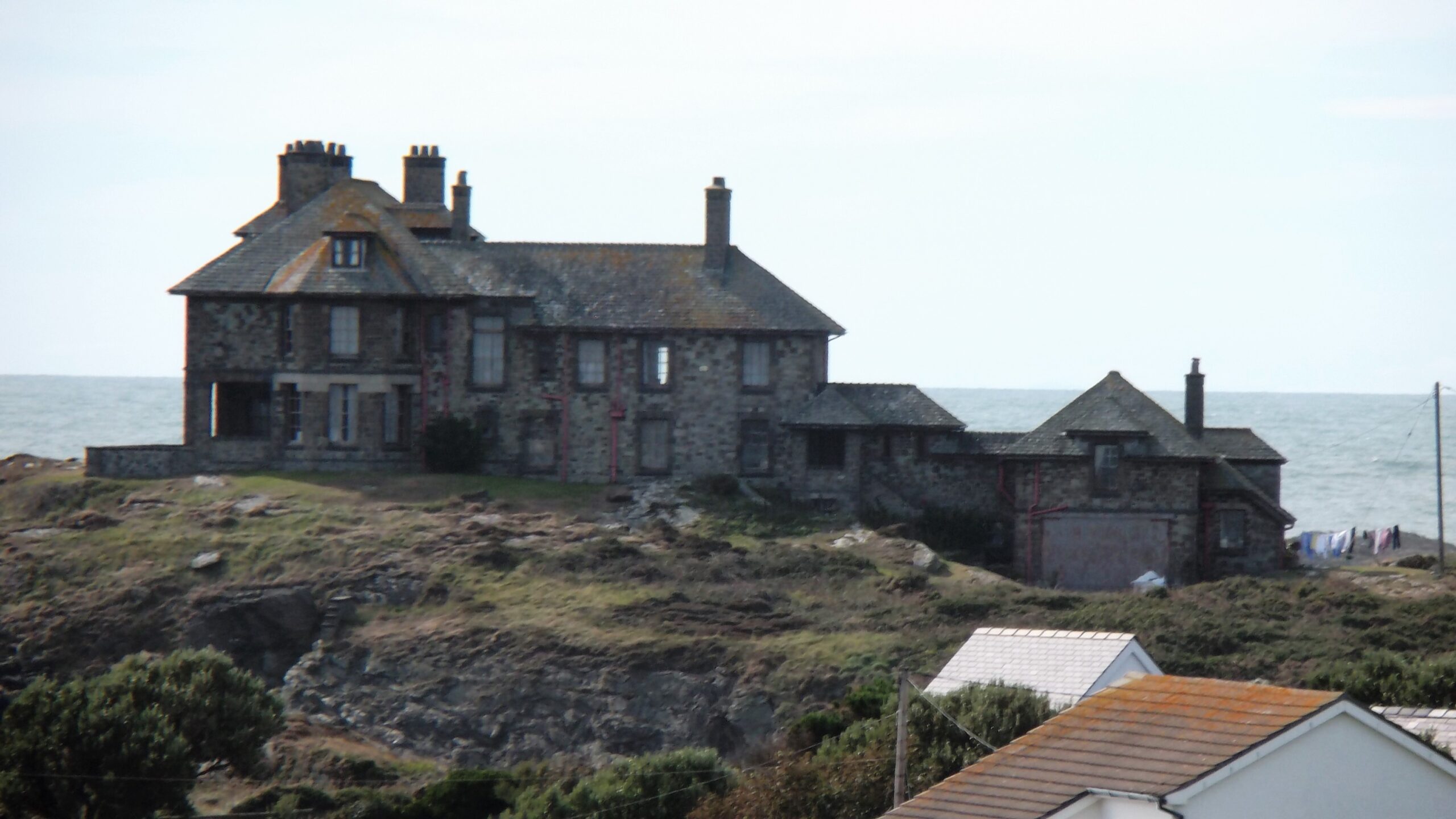 Photograph of an old, gray-brown house sitting near the shore