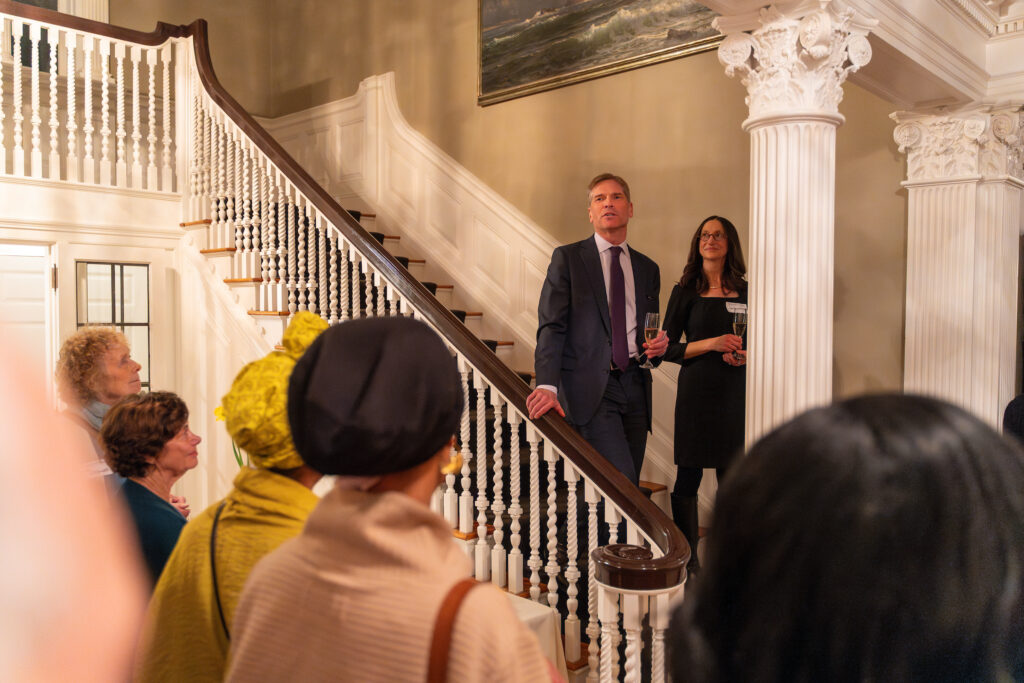 Acker and Elliott address a crowded foyer from the staircase.