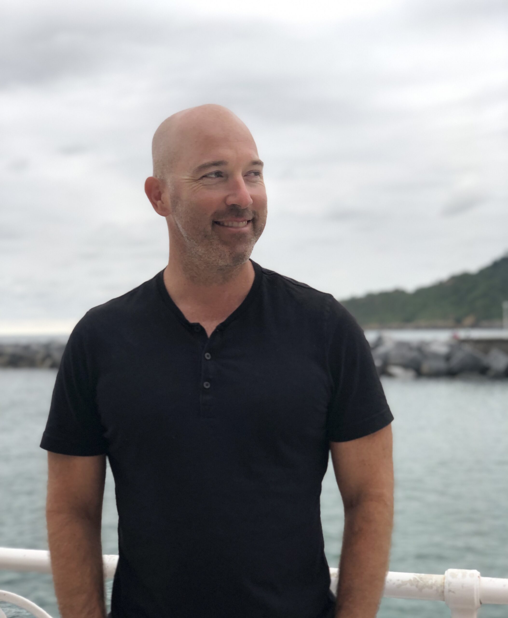 Julian Zabalbeascoa's headshot. A bald man with facial hair poses in front of a body of water, looking into the distance.